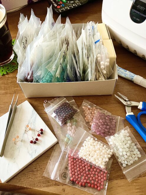 つぶつぶピアス用の丸いつぶつぶの半貫通天然石がギッシリ入った箱とつぶつぶピアス作製中の雑然とした机